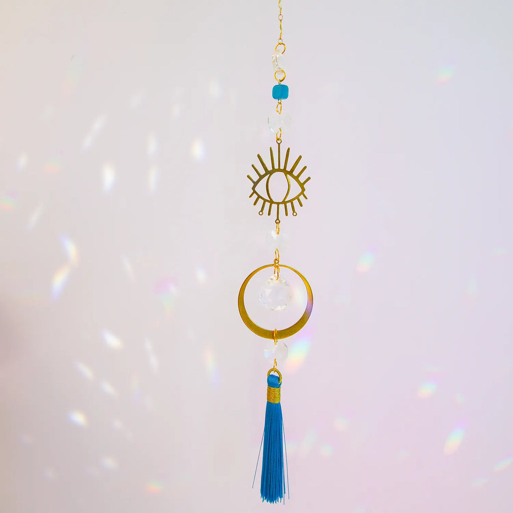 Eye-shaped handmade suncatcher by CocoMilkyWay with a blue tassel, symbolic decor piece capturing light and protection energy.
